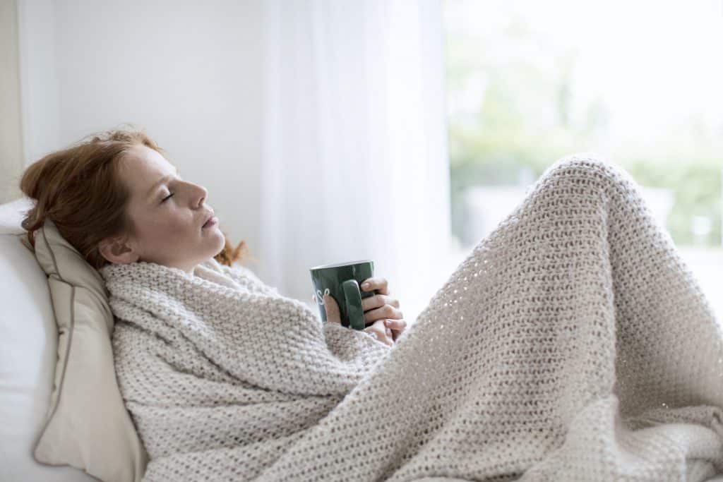 Frau erkältet unter der Decke mit Tasse Tee
