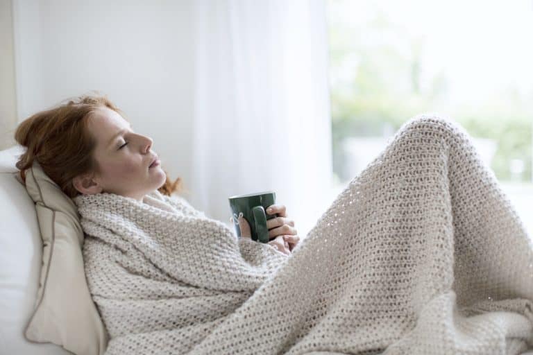 Frau erkältet unter der Decke mit Tasse Tee
