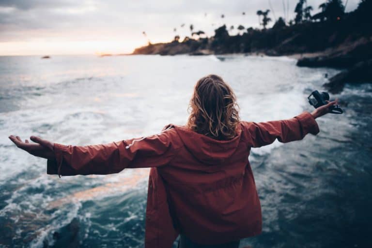 Mental Detox befreit: Eine Frau steht mit ausgebreiteten Armen am Strand und blickt zum Horizont.